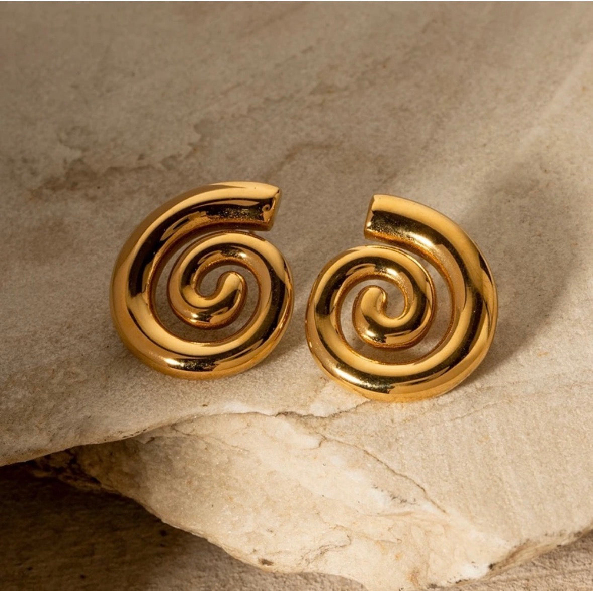 Gold plated spiral stud earrings on stone surface